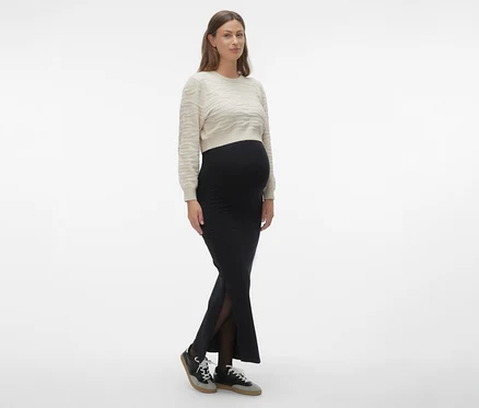 Žena má na sebe čiernu maxi sukňu MAMALICIOUS »MLEMMA TUBE«, svetlý sveter a tenisky.