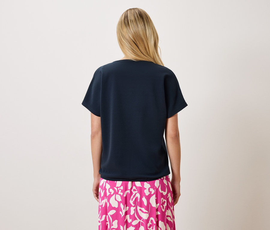 Pohľad zozadu na blondínku v tmavomodrom tričku a ružovej sukni s kvetinovou potlačou.