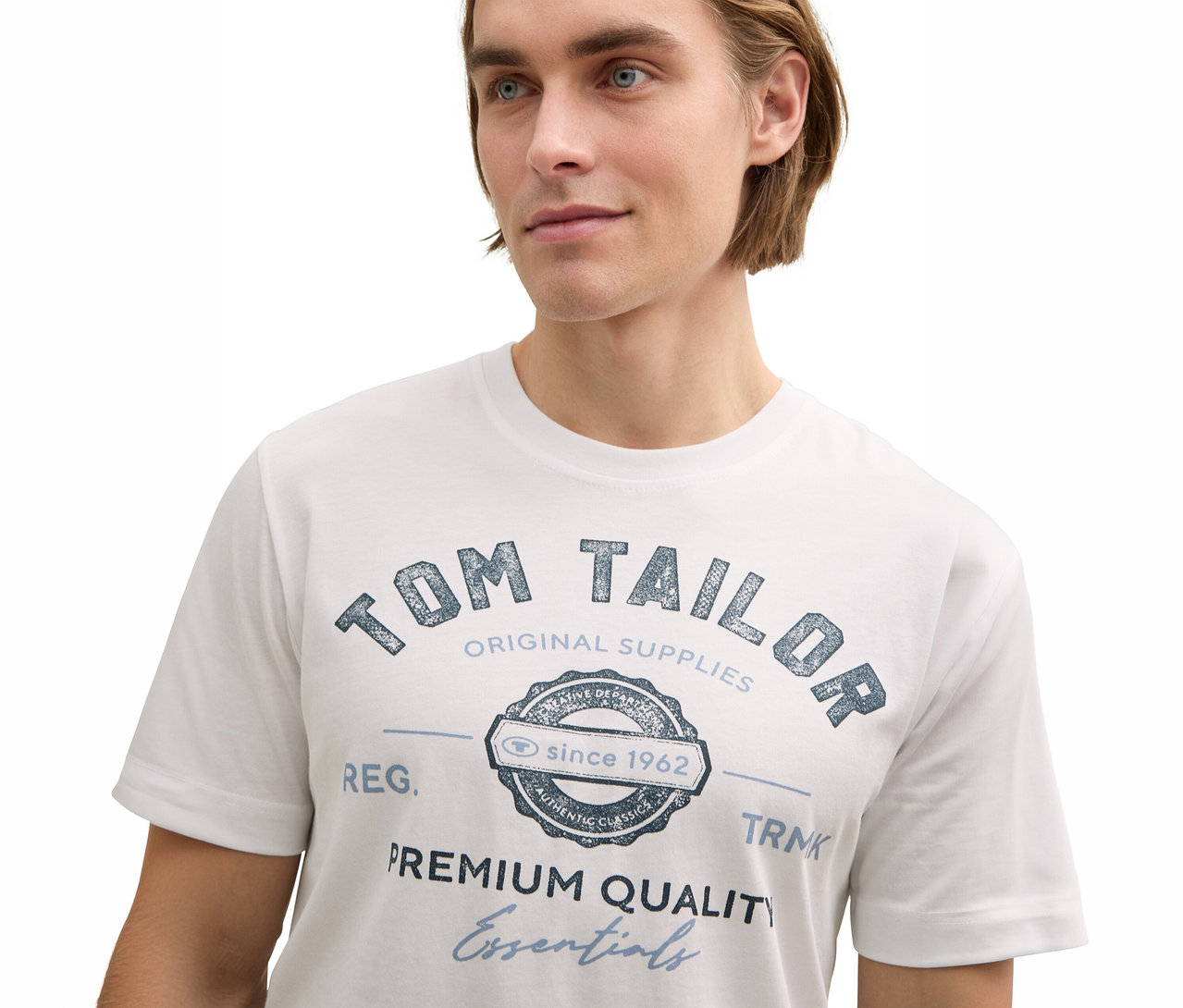 Muž má na sebe biele tričko Tom Tailor s logom.