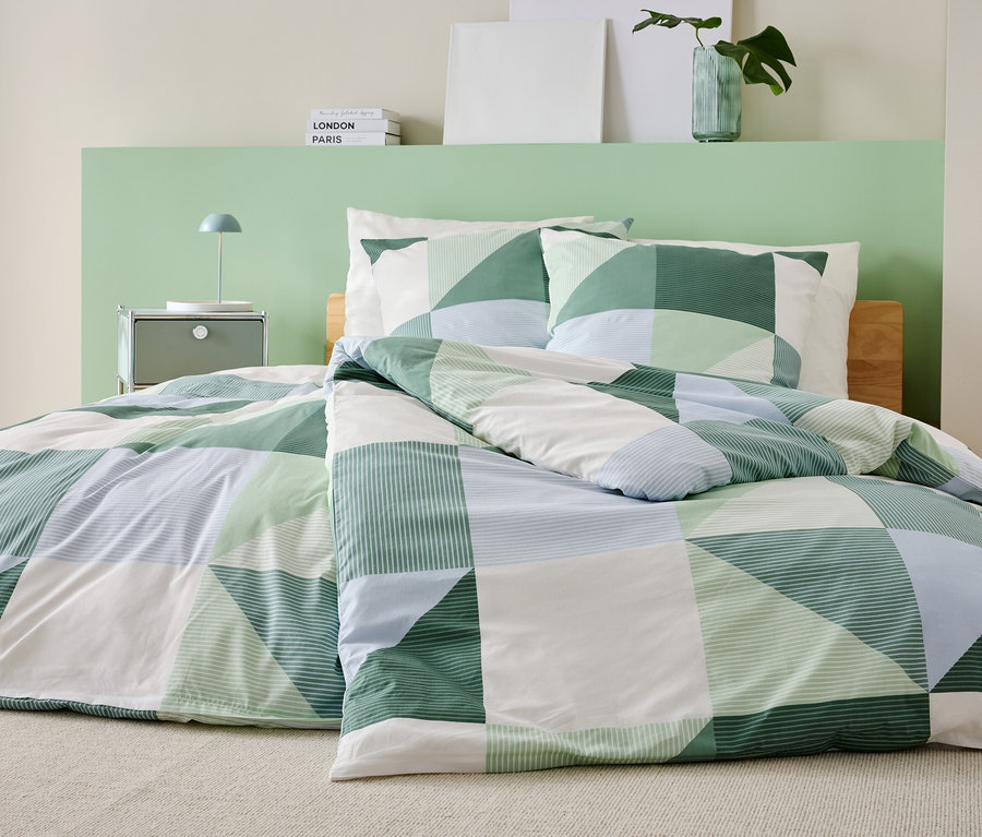 Posteľ so zeleno-bielo-modrou patchworkovou prikrývkou a ladiacimi obliečkami na vankúše stojí v spálni.