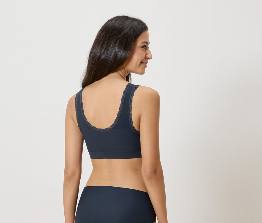 Žena má na sebe tmavomodrú podprsenku s čipkovaným lemom a zodpovedajúce spodné prádlo, pohľad zozadu.