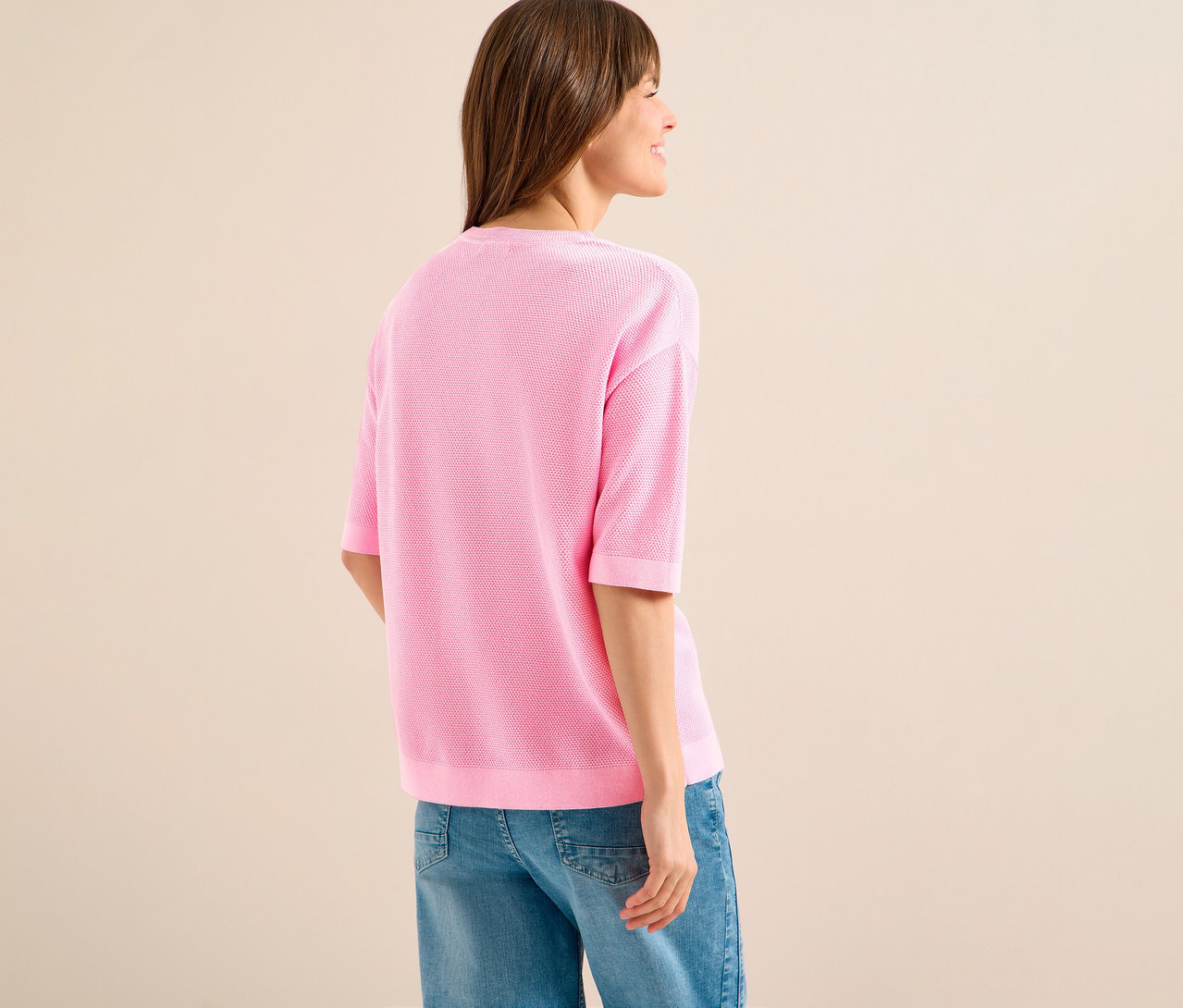 Žena zozadu v ružovom pulóvri s krátkym rukávom CECIL a džínsoch.
