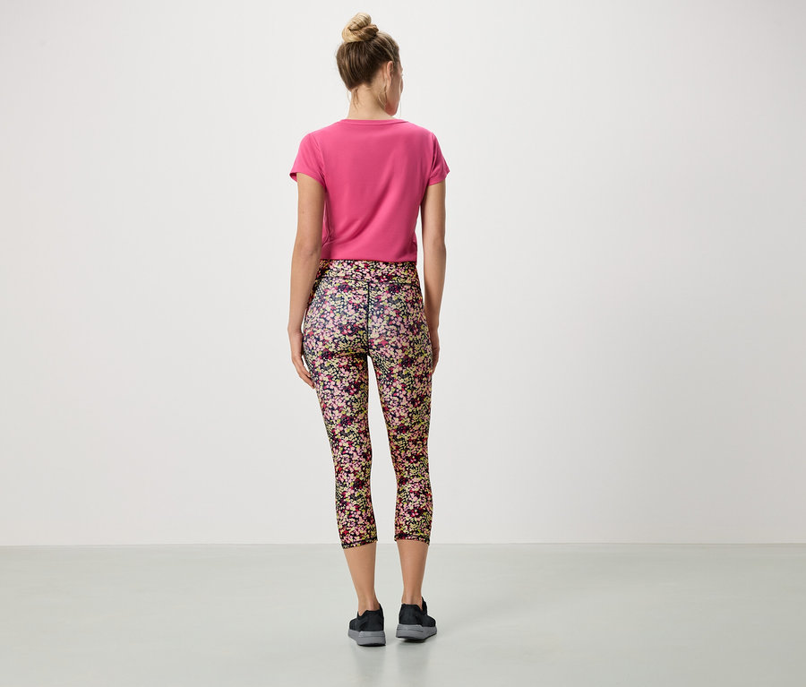 Pohľad zozadu na ženu s drdolom, ktorá má na sebe ružové tričko a kvetinové legíny.