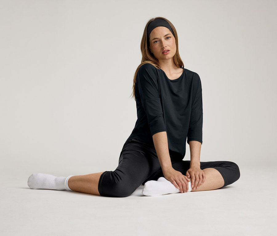Žena sedí v čiernom 3/4 športovom tričku. Má čelenku a biele ponožky.