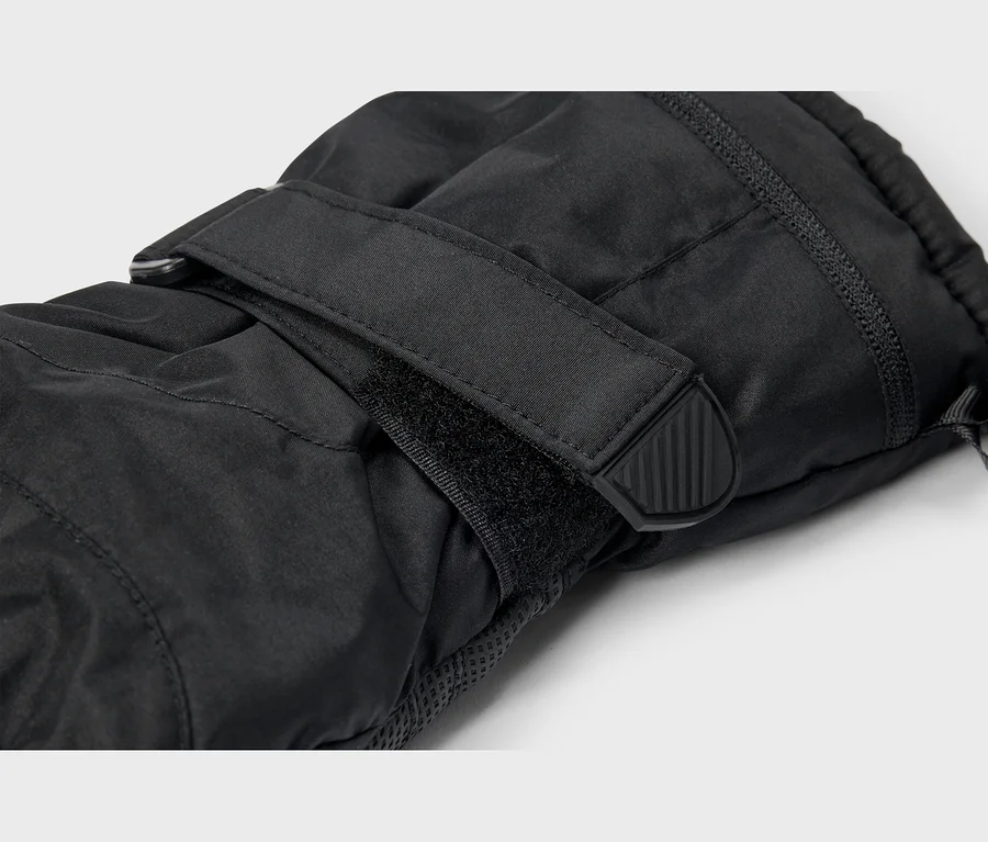 Detail čiernej rukavice s nastaviteľným remienkom na suchý zips okolo zápästia, s čiernym gumovým úchytom s vertikálnymi drážkami.
