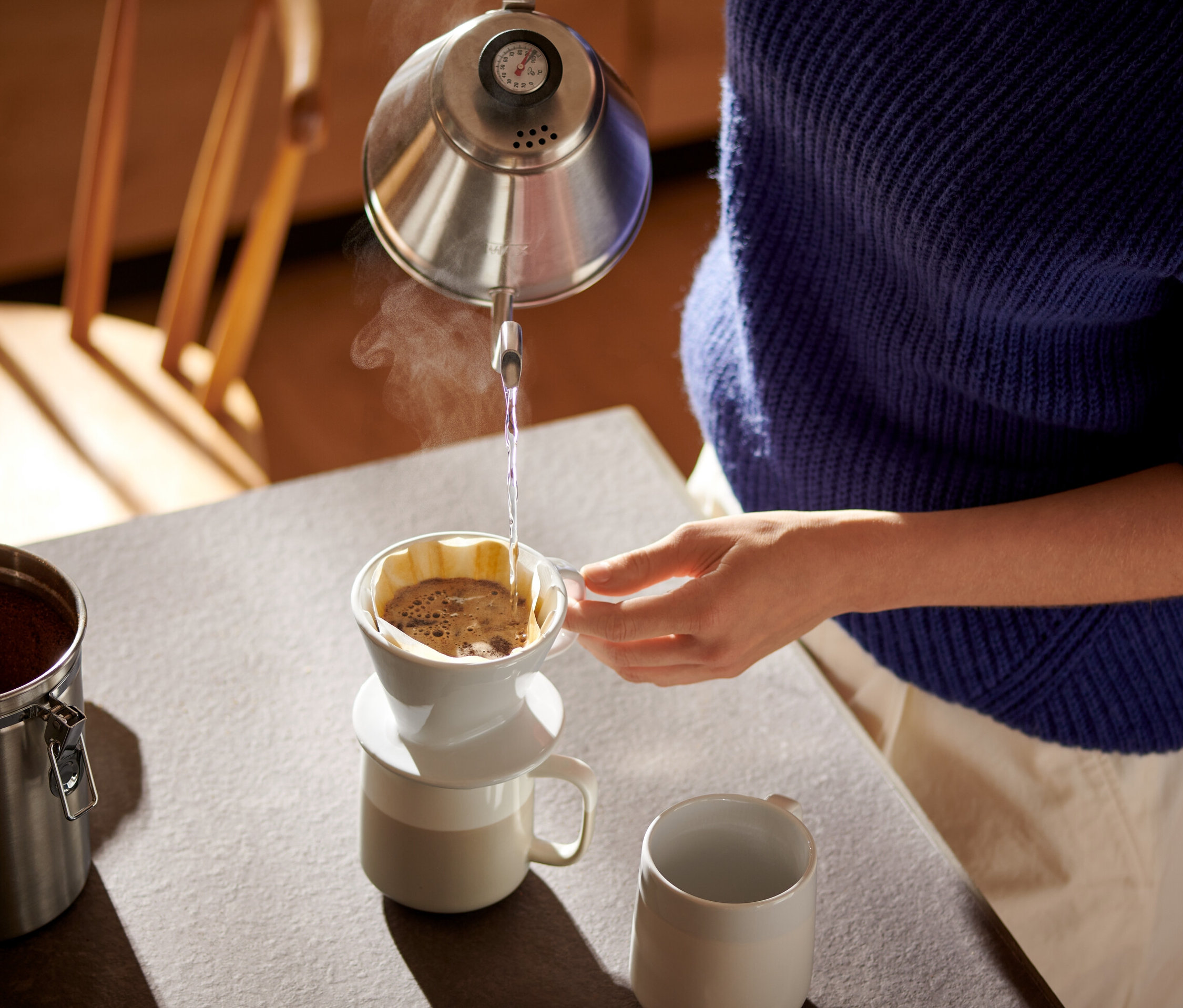 Žena naleje vodu z kanvice do bieleho ručného filtra na kávu veľ. 101 s papierovým filtrom na kávu veľ. 101.