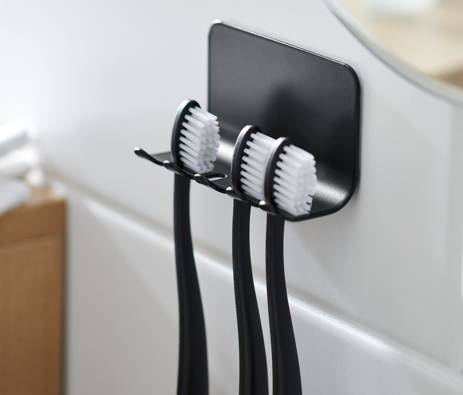 Čierny držiak na zubné kefky s tromi zubnými kefkami na bielych dlaždiciach.