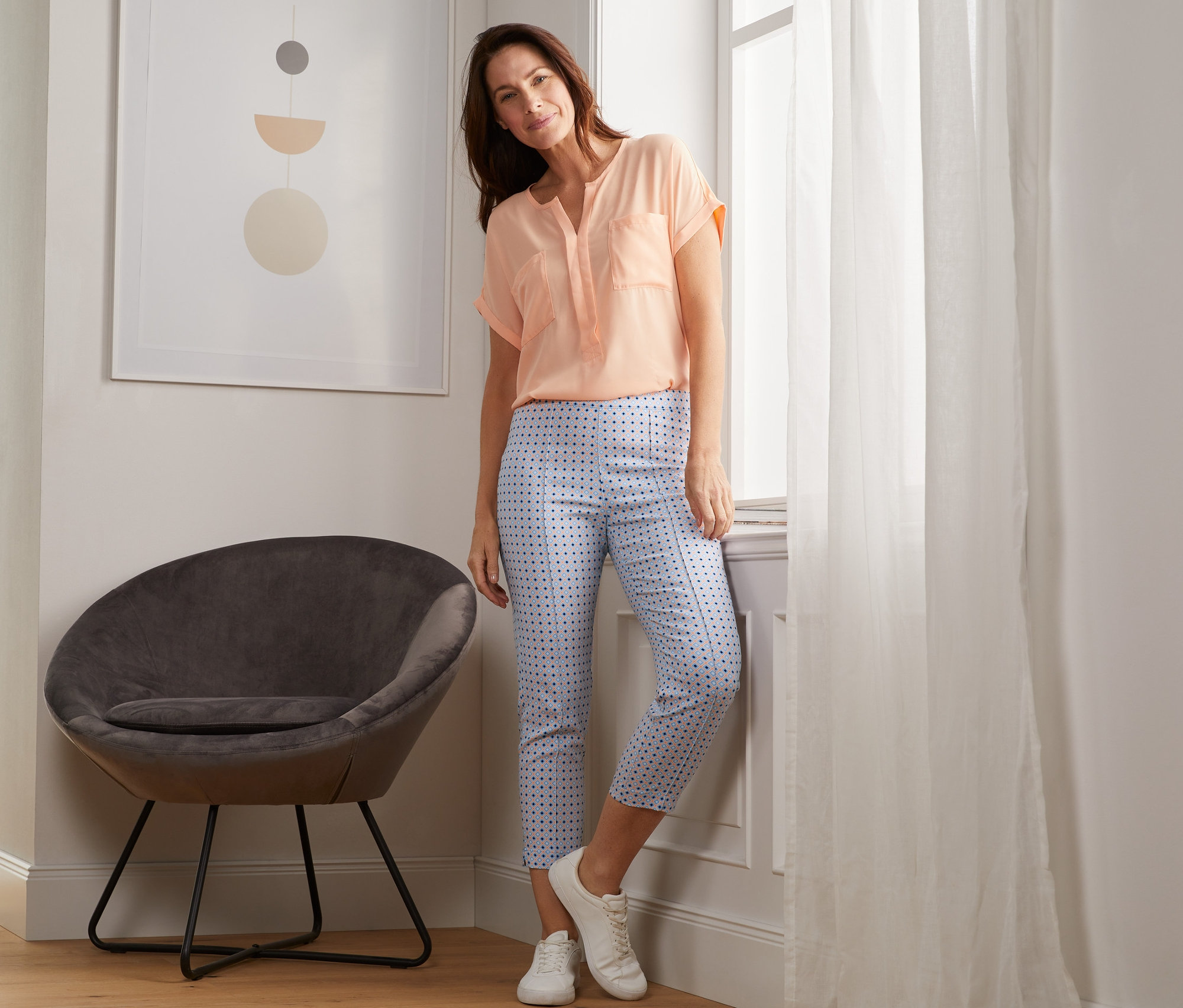 Žena opretá o okno pózuje v sedemosminových elastických nohaviciach s potlačou.