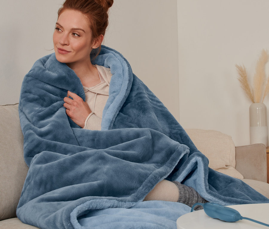 Žena sedí na pohovke zabalená vo vyhrievacej deke.