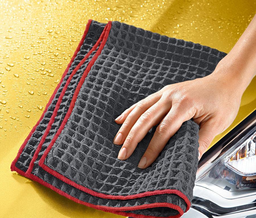 Ruka utiera žltú kapotu auta špeciálnou handričkou na utieranie dosucha.