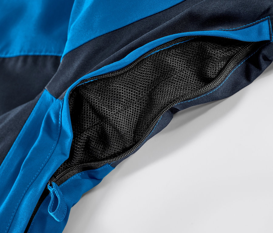 Detail modrej lyžiarskej bundy s otvoreným vreckom na zips.