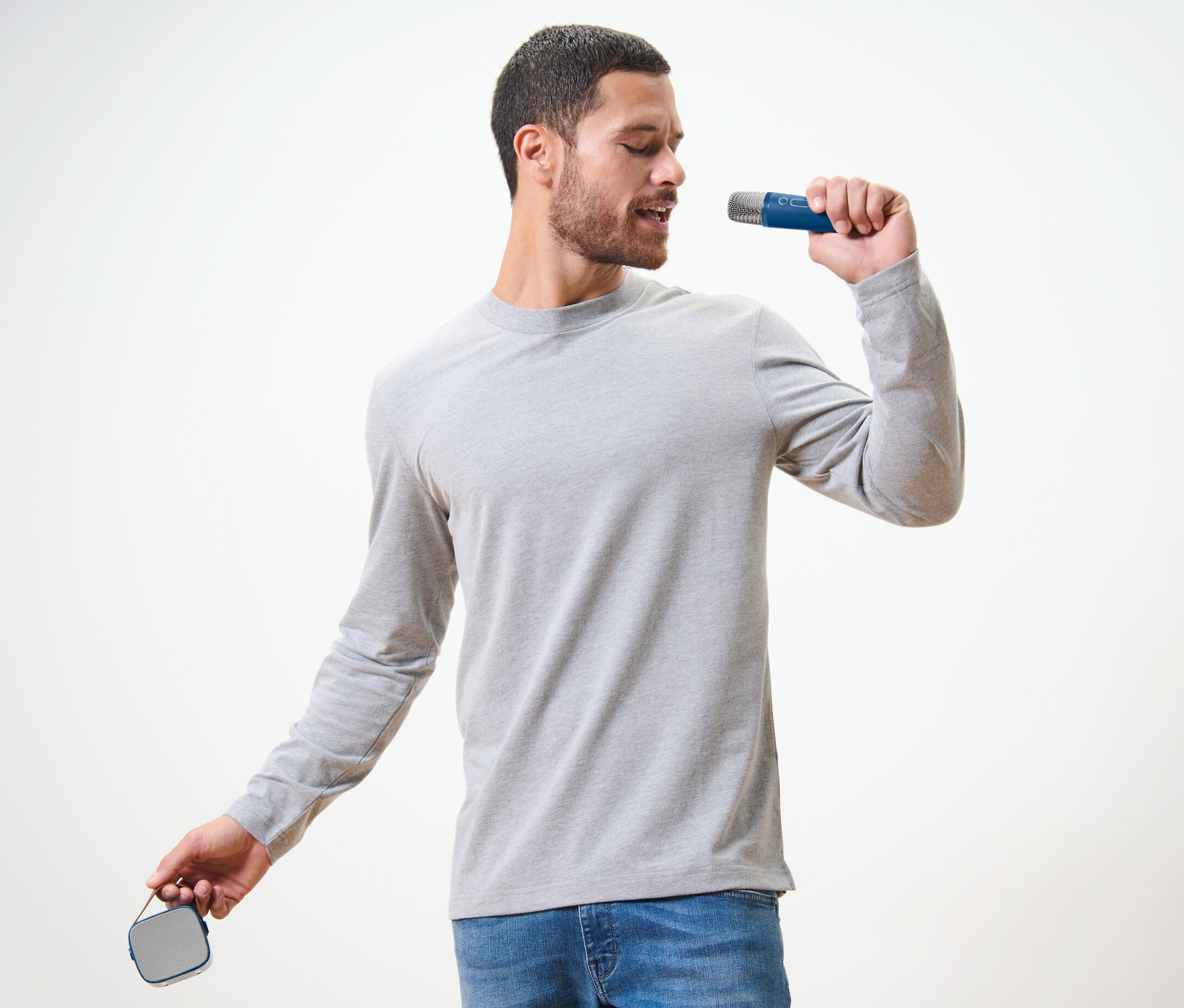 Muž spieva do mikrofónu zo súpravy na karaoke s reproduktorom.