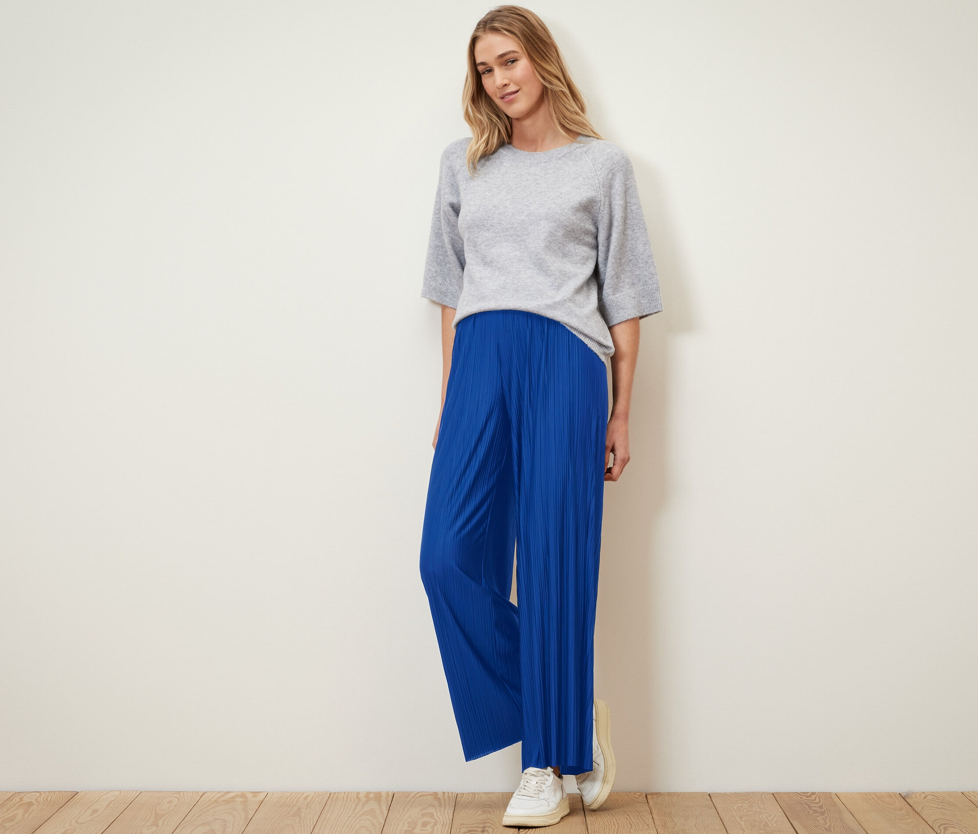 Žena stojí a má na sebe plisované nohavice kobaltovomodrej farby a sivý top.