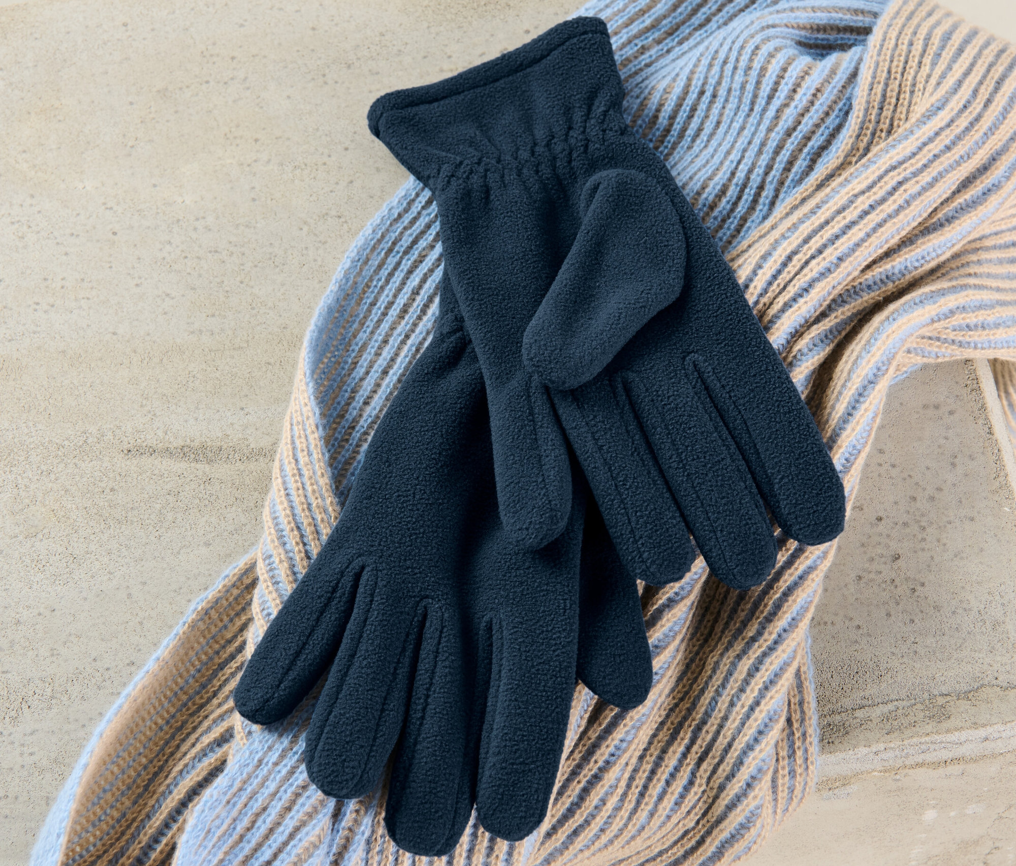 Pár flaušových rukavíc leží na šále.