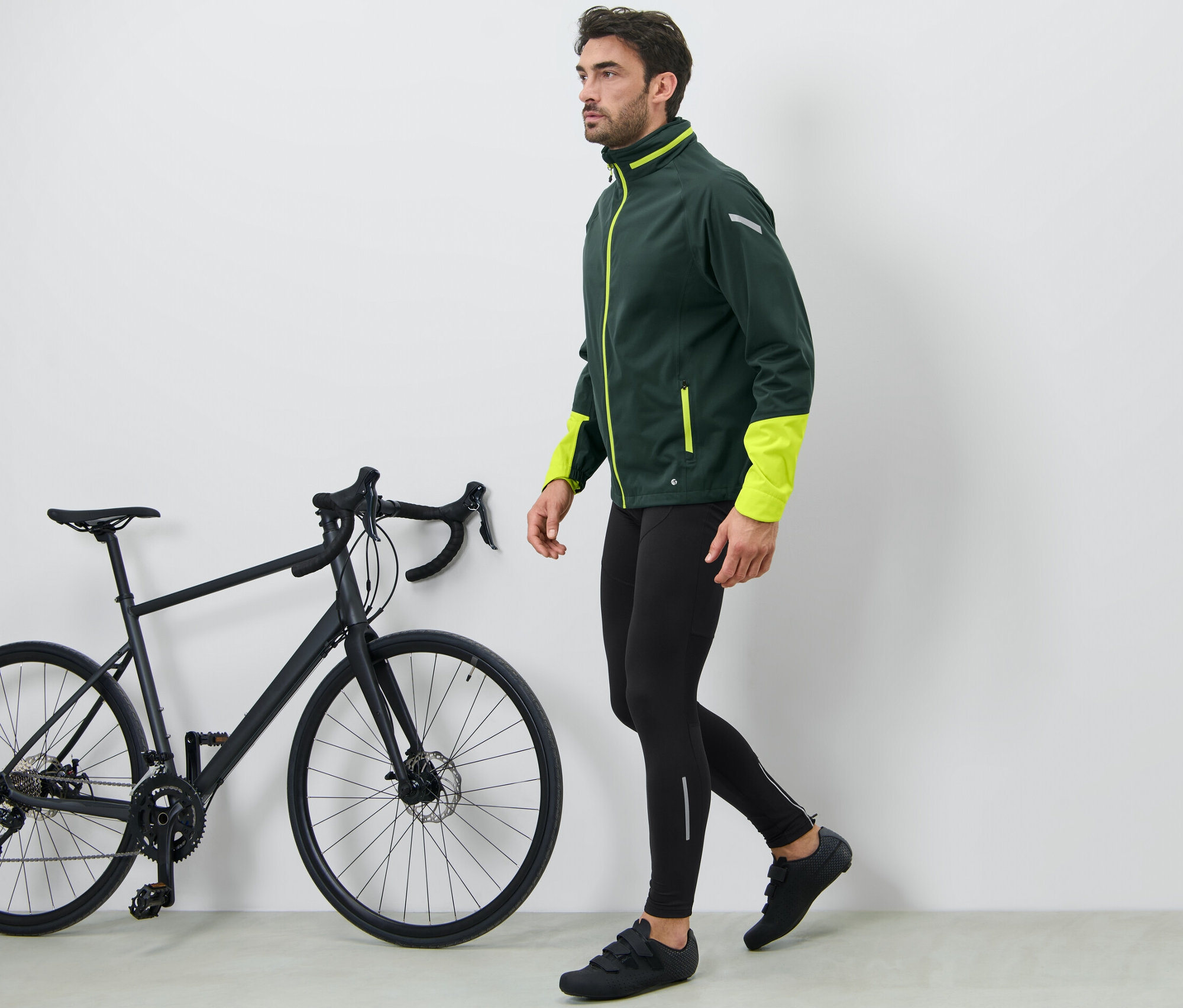 Muž kráča vedľa čierneho bicykla a má na sebe cyklistické nohavice.