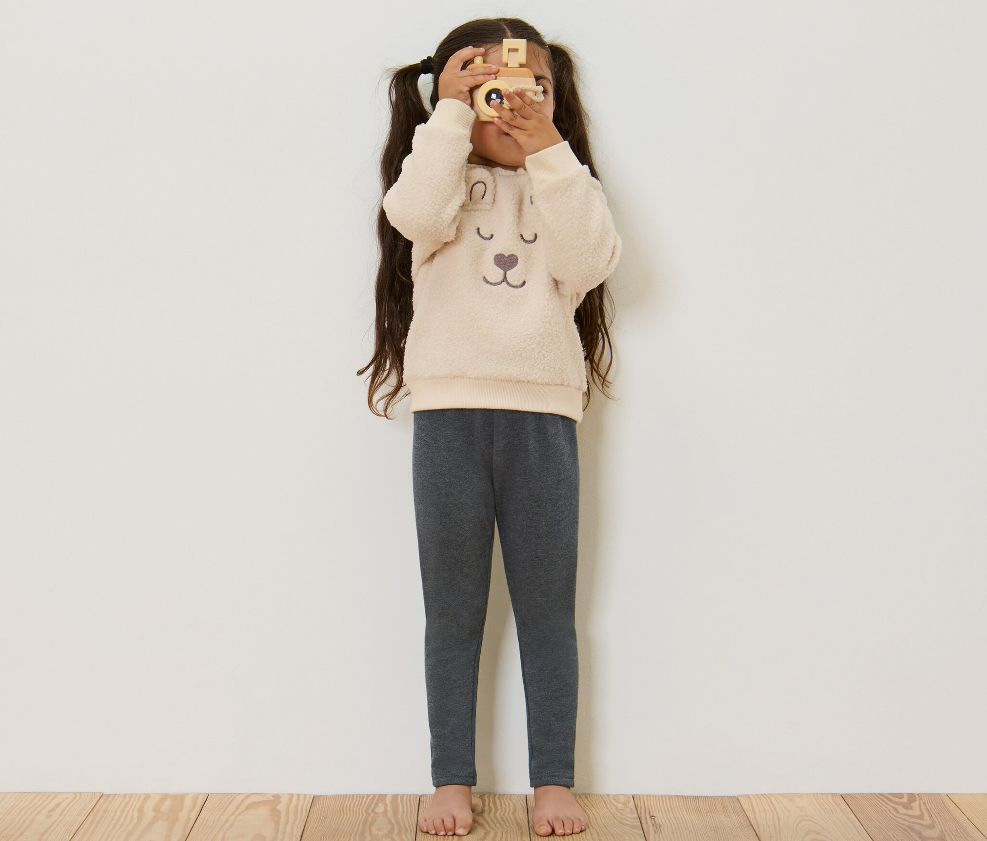 Dievča sa pozerá cez drevený fotoaparát a má na sebe sivé detské termo legíny.