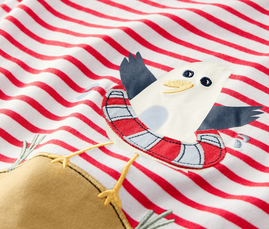 Detail detského trička s červenými pruhmi a aplikáciou čajky s plávacím kruhom.