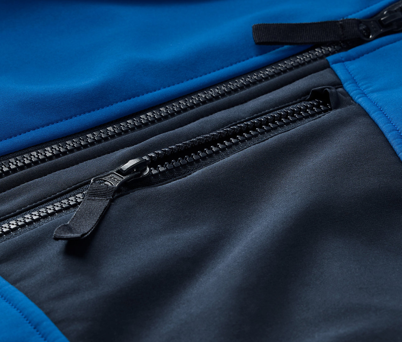 Detail modro-čiernej softshellovej bundy so zipsami.