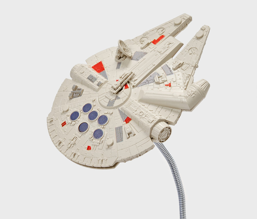 Model lode Millennium Falcon s detailmi červenej a šedej farby, pripevnený na ohybnom striebornom stonke.