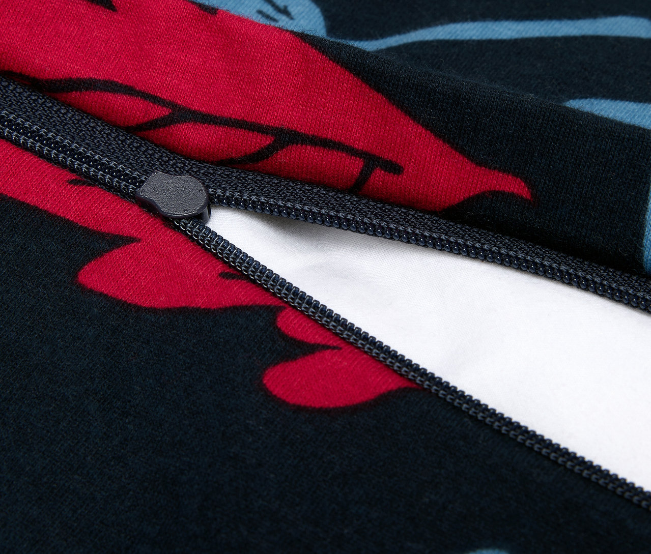 Detailný záber na zips na tmavomodrej obliečke na paplón s červenými a modrými kvetmi.