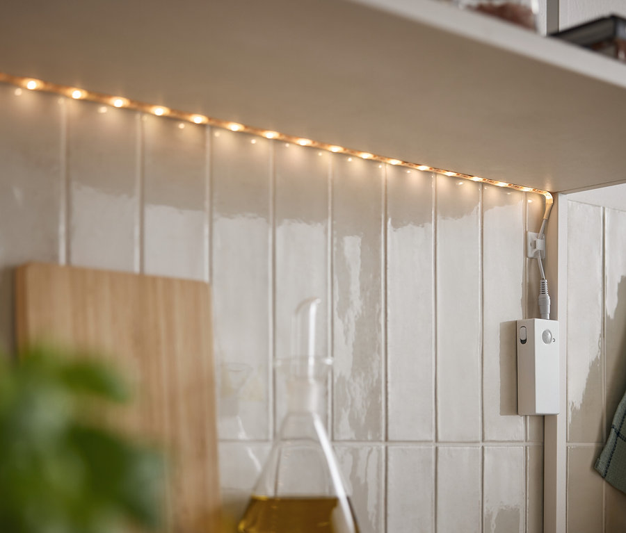 LED pásik svieti pod skrinkou na bielych dlaždiciach.