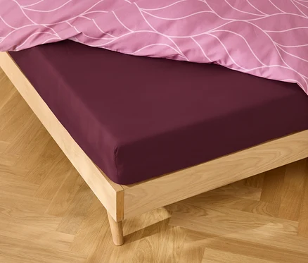 Detail postele s bordovou plachtou a ružovou vzorovanou posteľnou bielizňou.