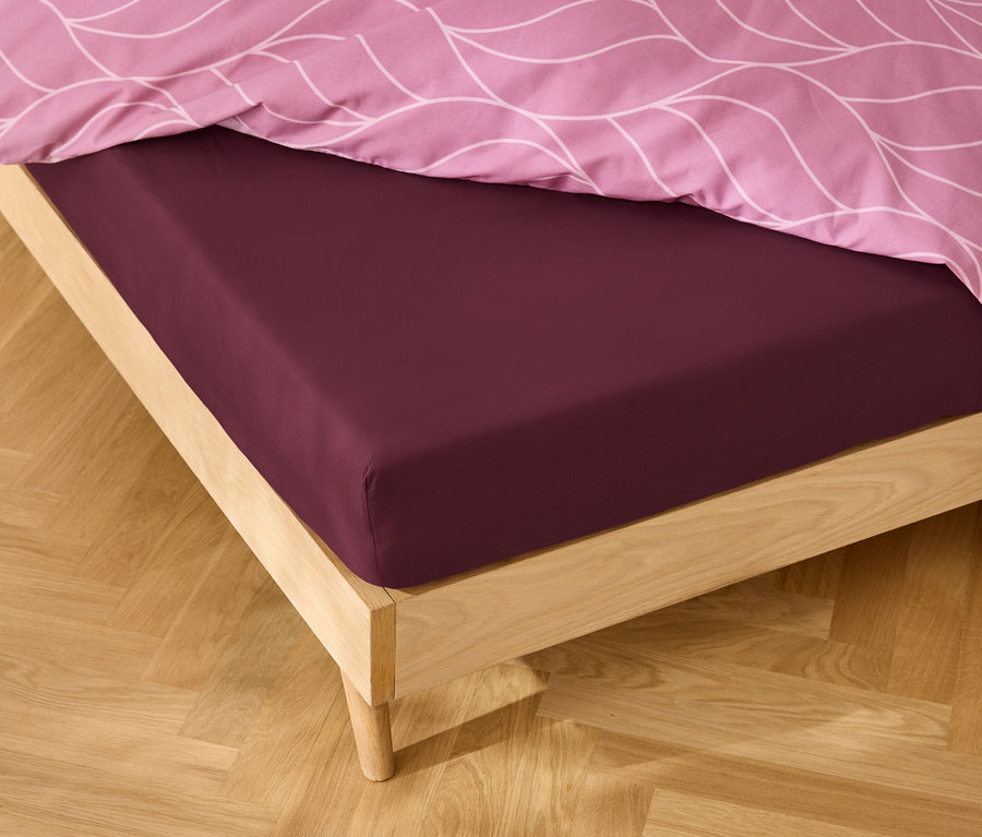 Detail postele s bordovou plachtou a ružovou vzorovanou posteľnou bielizňou.