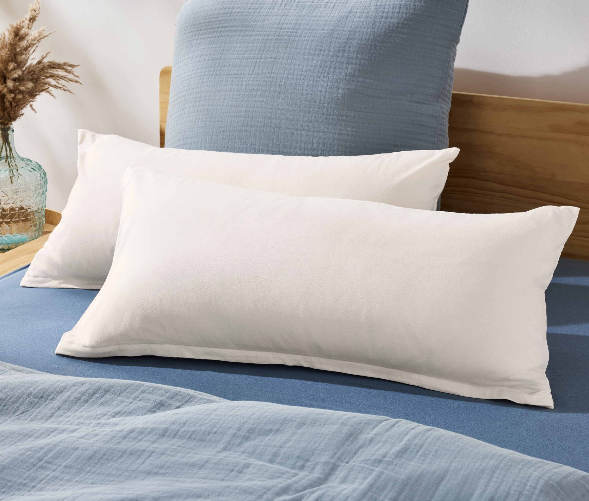 Dve džersejové obliečky na vankúše ležia na posteli s modrou plachtou a prikrývkou.