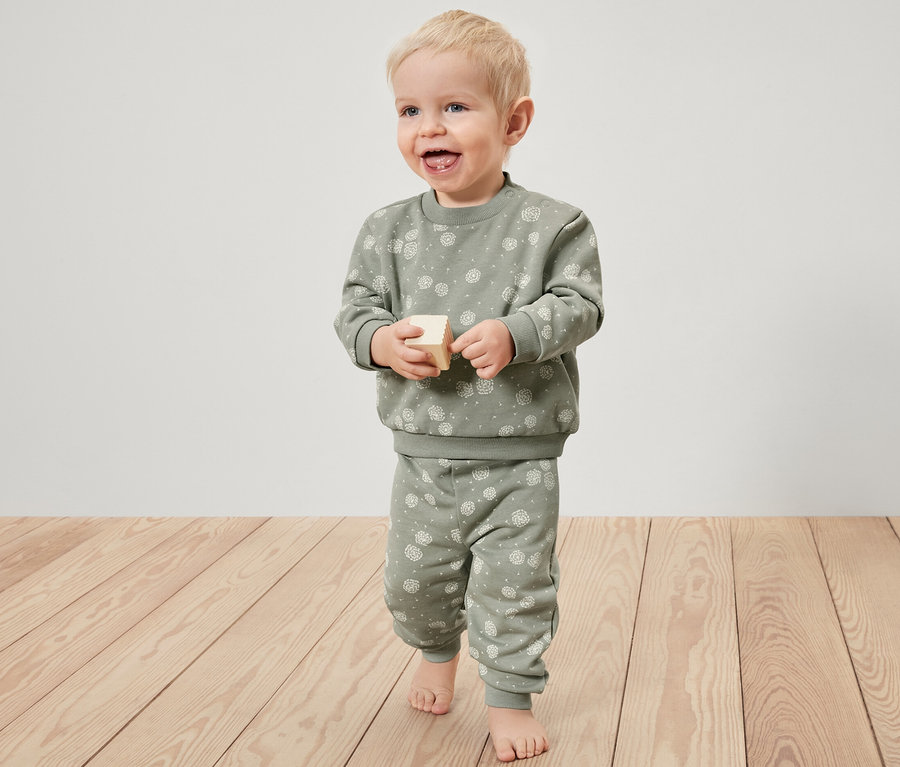 Dieťa sa hrá s drevenou kockou a má na sebe teplákovú súpravu.