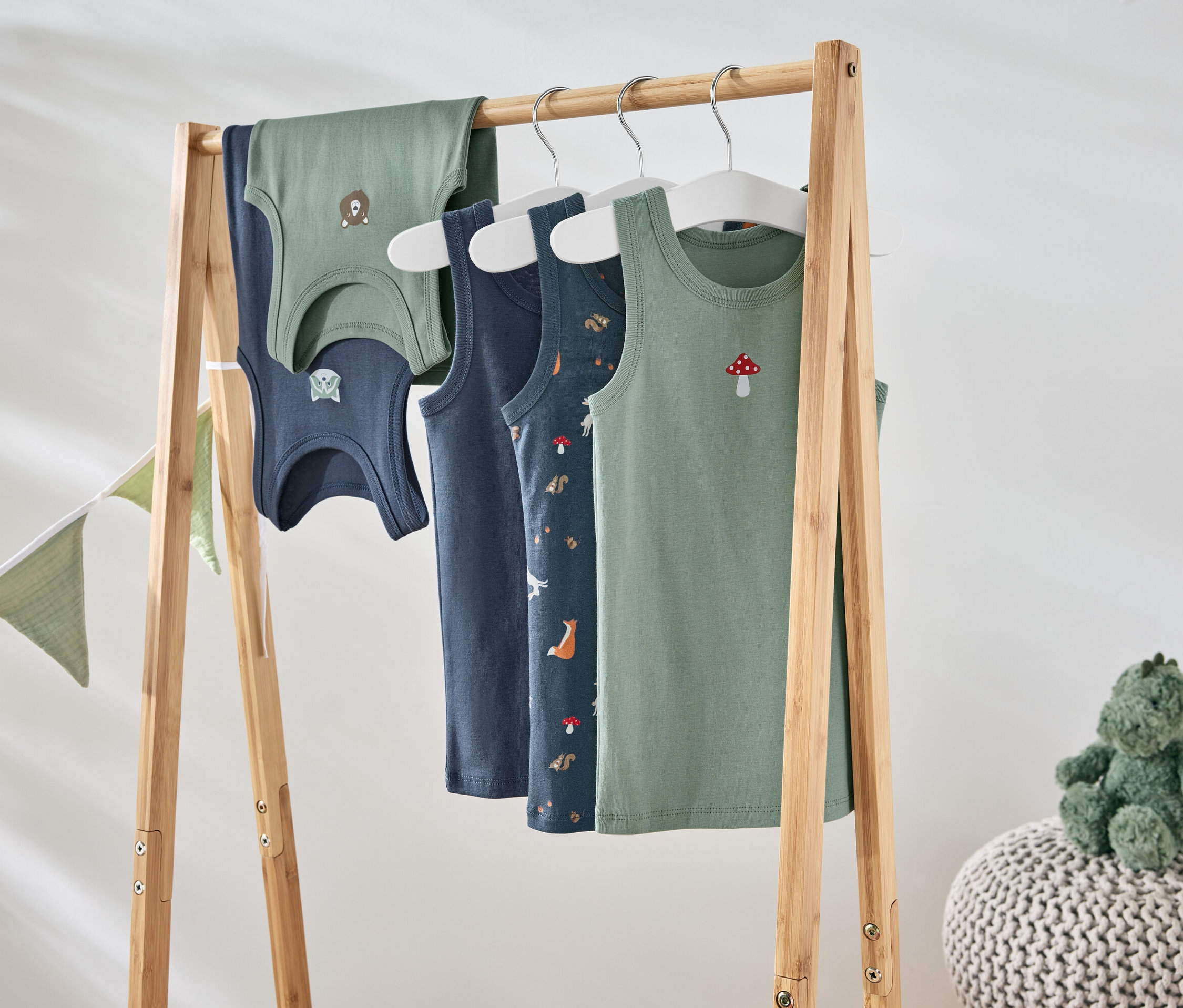 Štyri tielka s rôznymi motívmi visia na drevenom stojane.