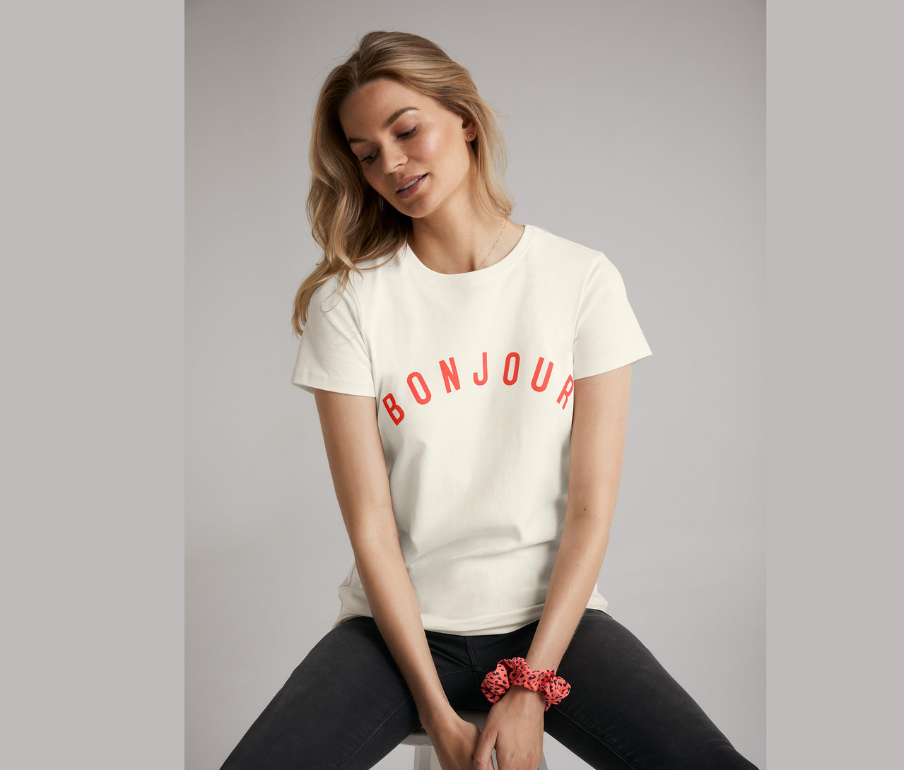 Žena sedí na stoličke v úzkych džínsoch a tričku s potlačou.