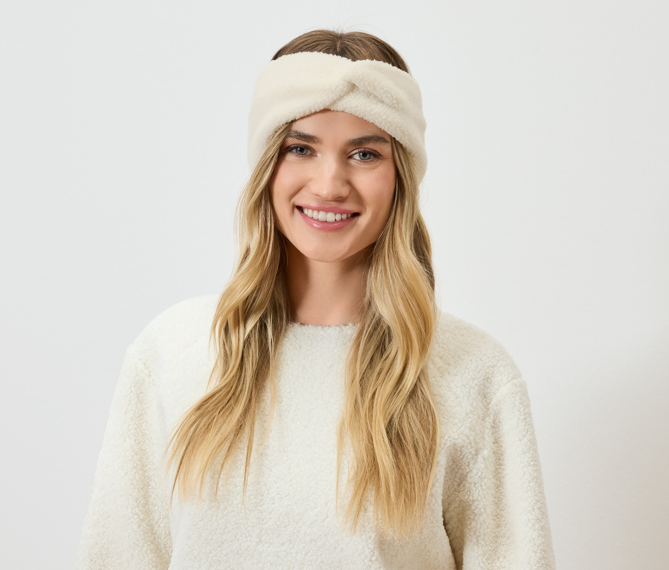 Portrét usmievavej ženy s blond vlasmi a krémovou čelenkou a svetrom.