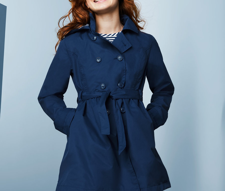 Usmievajúce sa dospievajúce dievča pózuje v modrom trenčkote do každého počasia s recyklovaného materiálu.