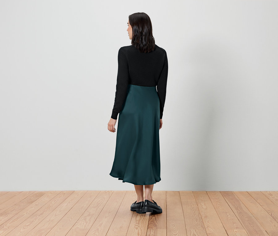 Žena stojí chrbtom a má na sebe čierny top a zelenú sukňu.