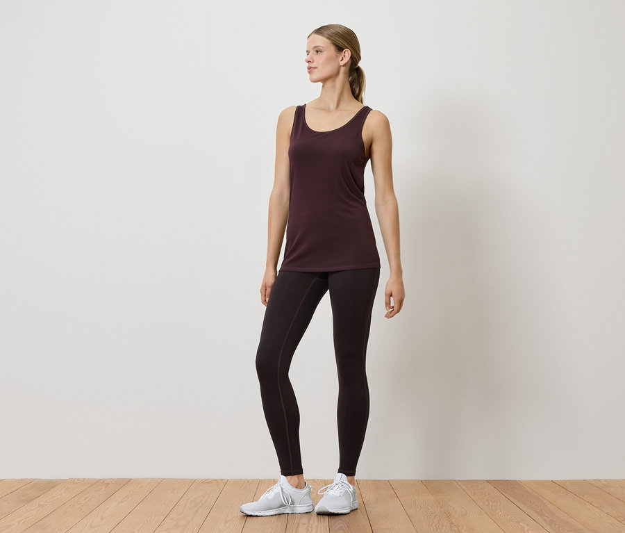 Žena v tielku a legínach pózuje v interiéri.