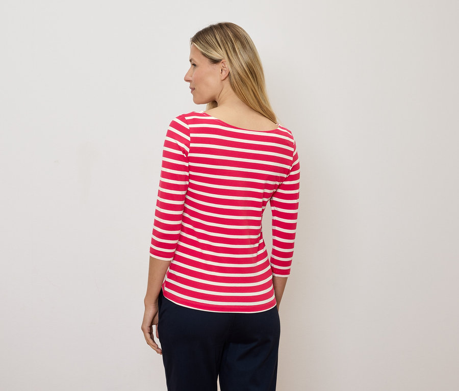 Blondína sa pozerá doľava a má na sebe červeno-biele pruhované tričko s trojštvrťovým rukávom.