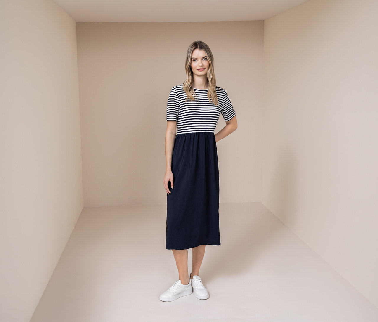 Žena v šatách Street One s modro-bielym pruhovaným topom a modrou sukňou a bielymi teniskami.