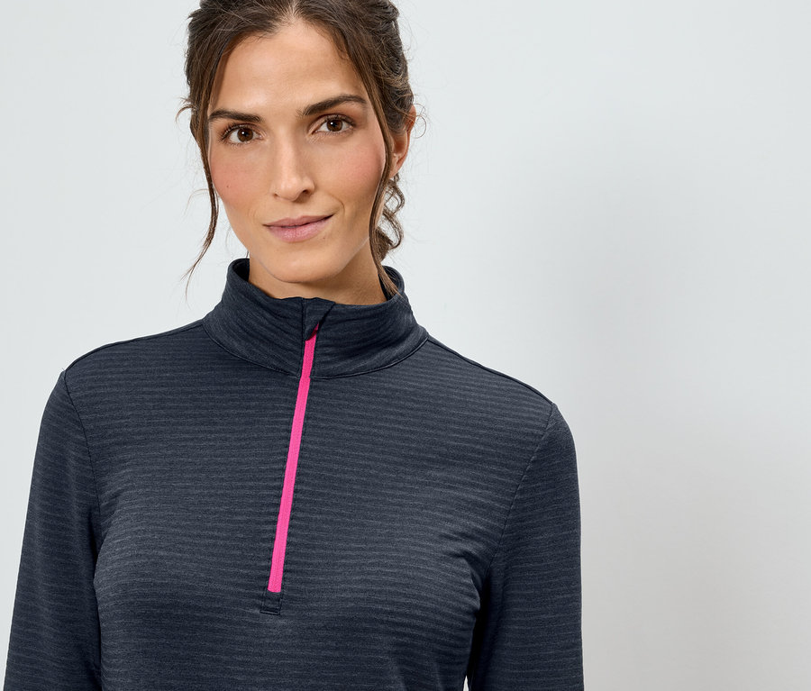 Žena má na sebe tmavomodrý top s dlhým rukávom a ružovým zipsom.