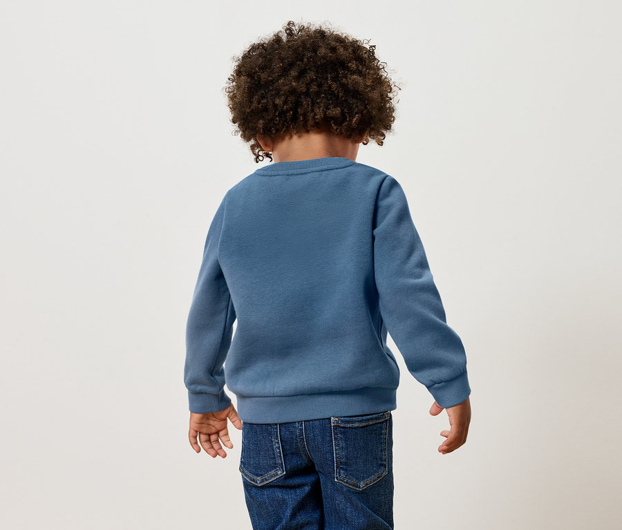 Pohľad zozadu na dieťa s kučeravými vlasmi v modrom svetri a džínsoch.