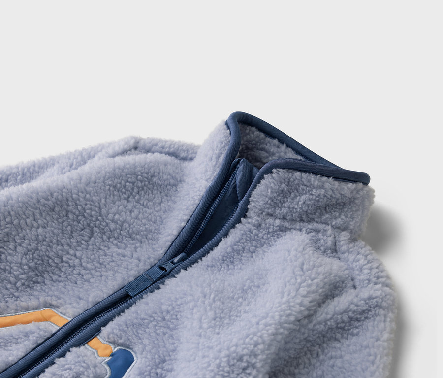 Detailný záber na svetlomodrú fleecovú bundu s modrým zipsom.