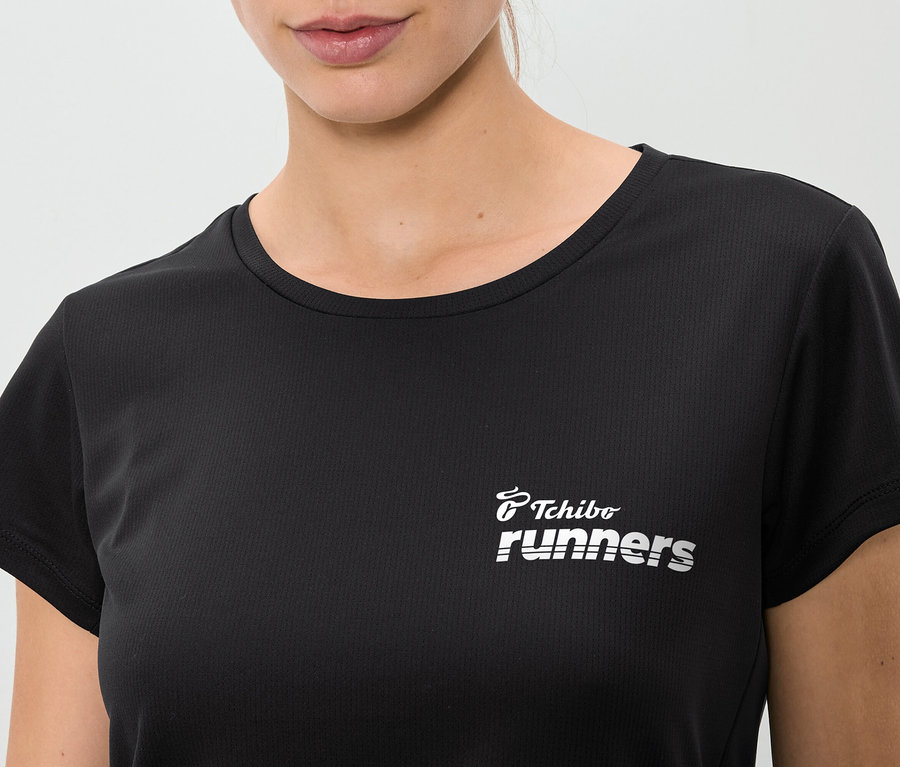 Detail ženy v čiernom tričku s nápisom "Tchibo runners".