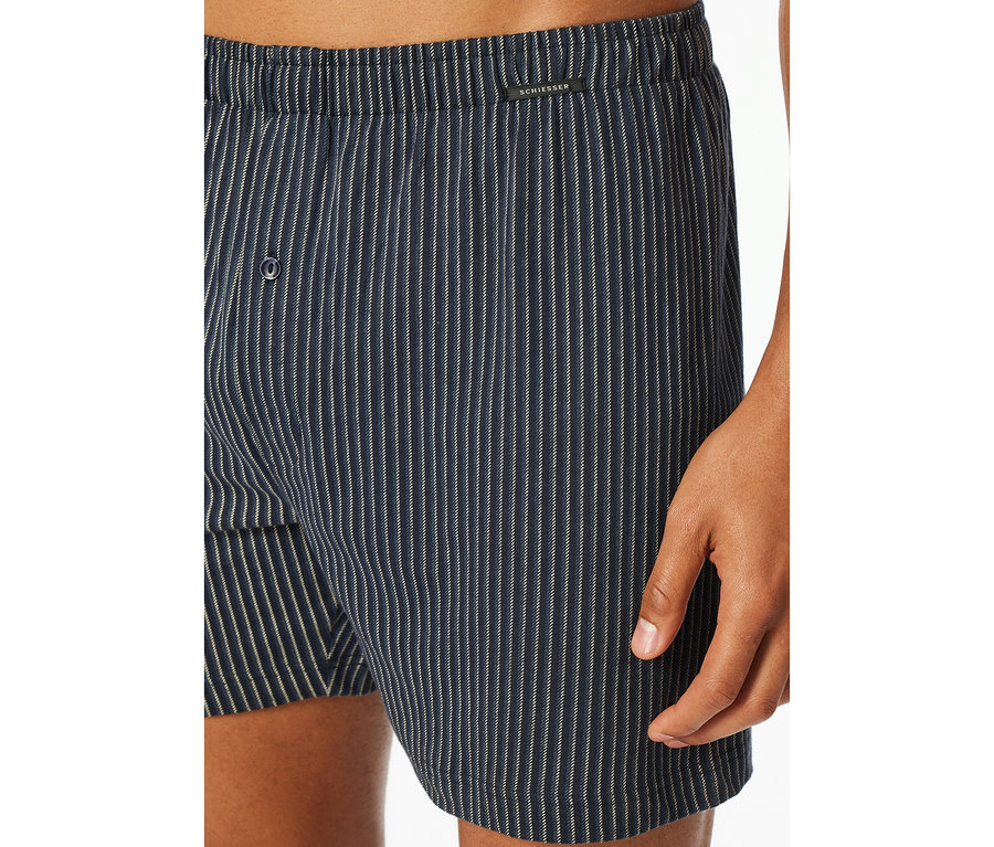 Detail osoby v modro-bielych pruhovaných džersejových boxerkách SCHIESSER s gombíkovým rázporkom.