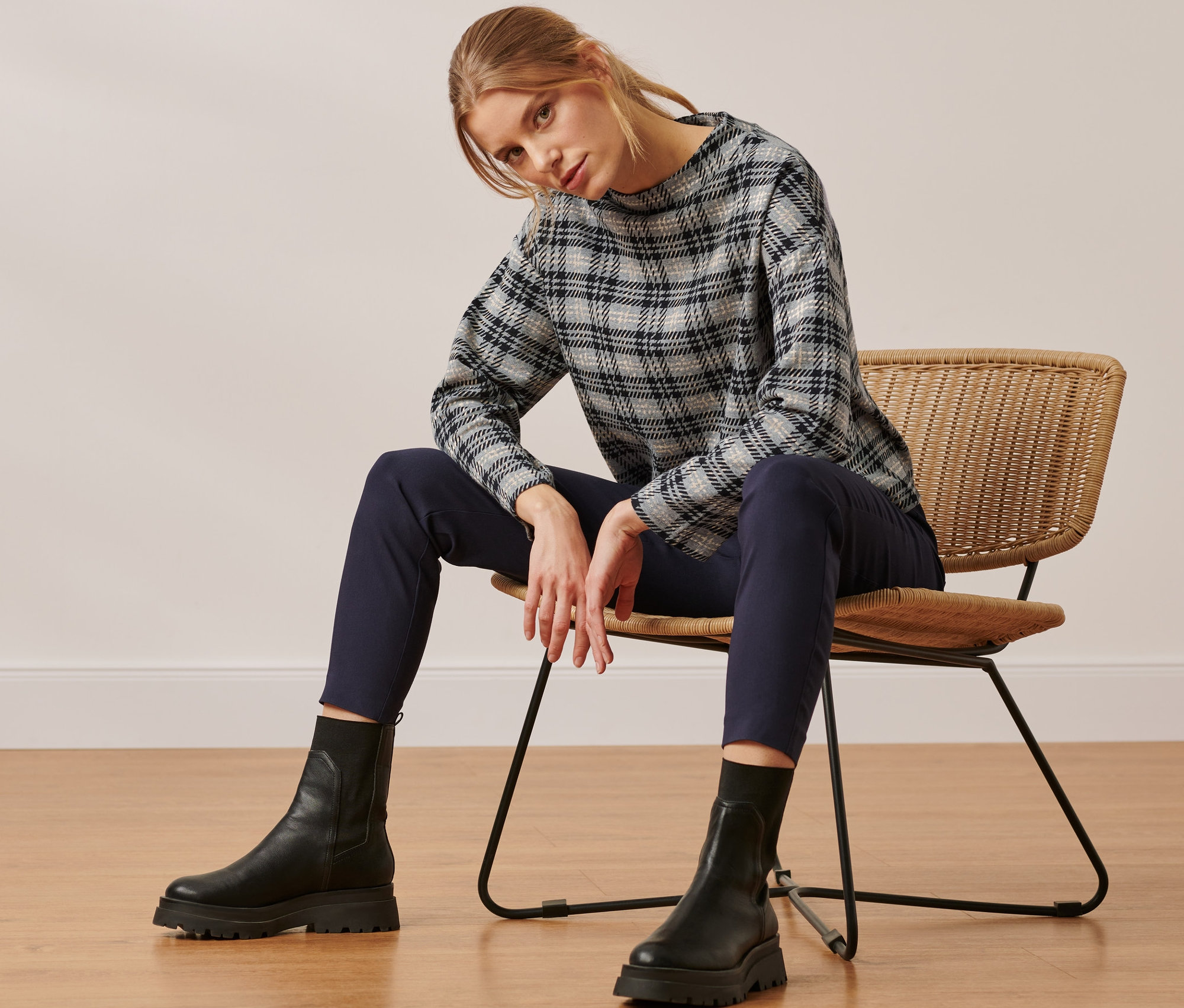 Žena sedí na prútenej stoličke a má na sebe kockovanú mikinu.