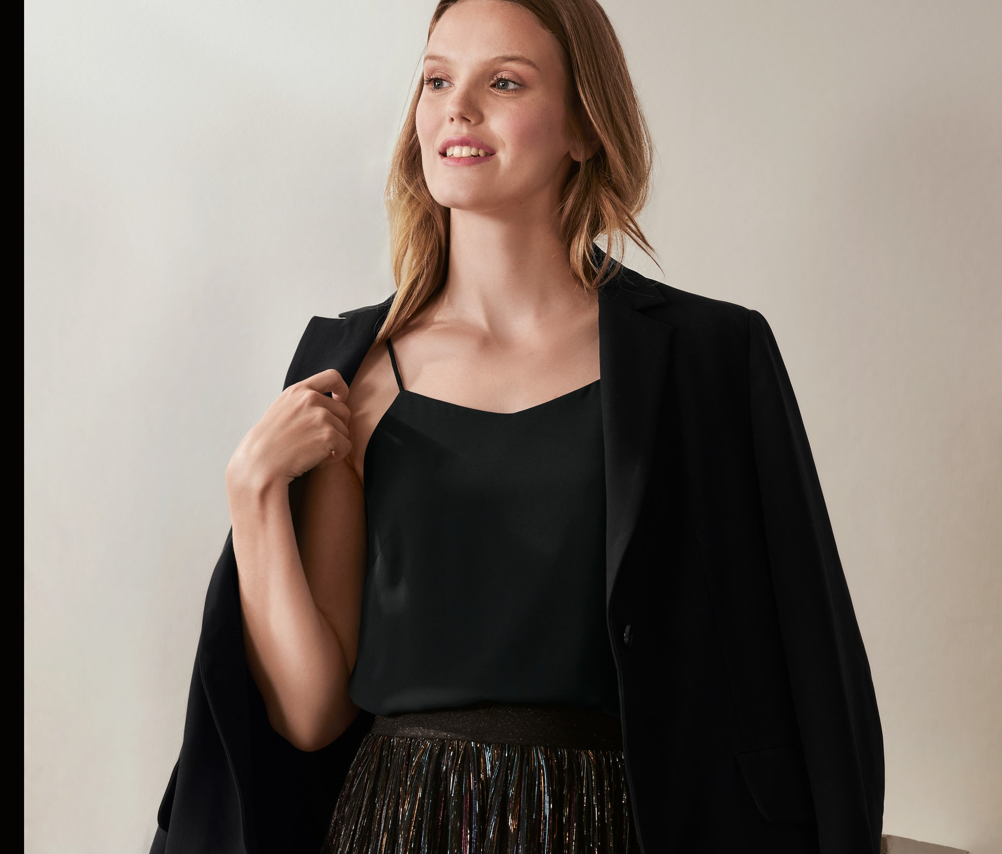 Žena má na sebe saténový top, sako a sukňu.