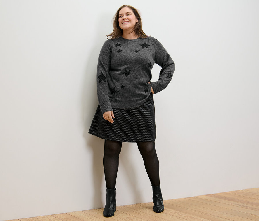 Žena pózuje v pletenom pulóvri a trblietavej žakárovej sukni.