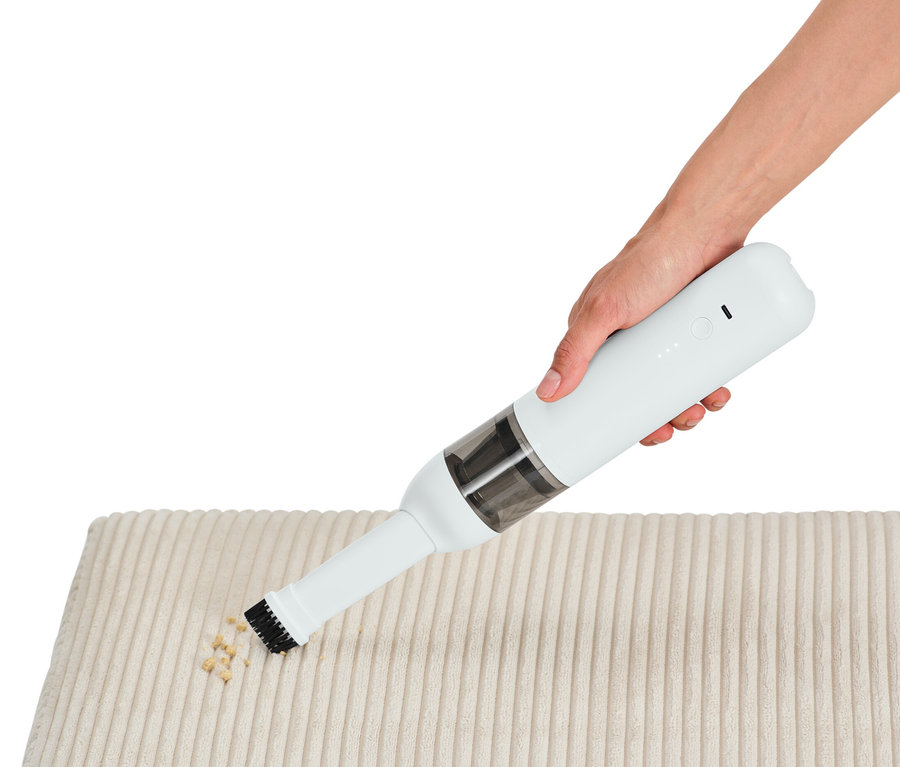 Ruka používa akumulátorový ručný vysávač na čistenie krémovej látky od omrviniek.