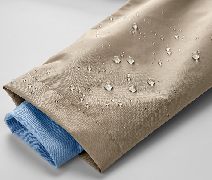 Detail detskej hnedej bundy do dažďa s kvapkami vody a modrým rukávom košele.