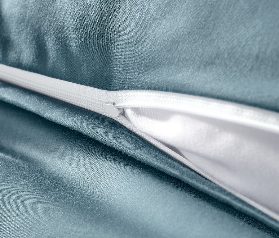Detail modrej posteľnej bielizne z bavlneného saténu s bielym zipsom.