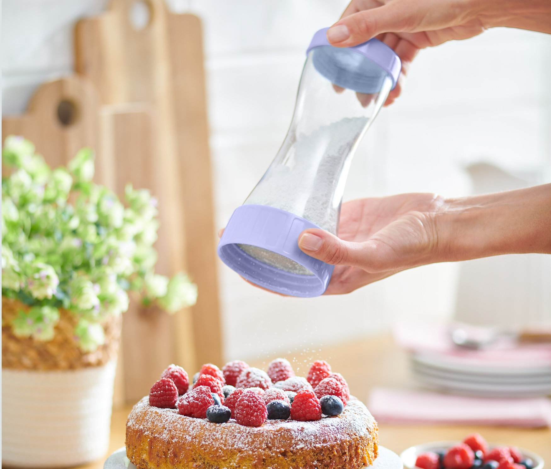 Žena sype práškový cukor z cukorničky na práškový cukor na tortu s ovocím.