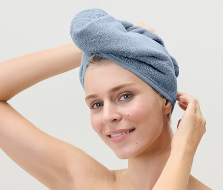 Žena si upravuje svetlomodrý uterákový turban na hlave.